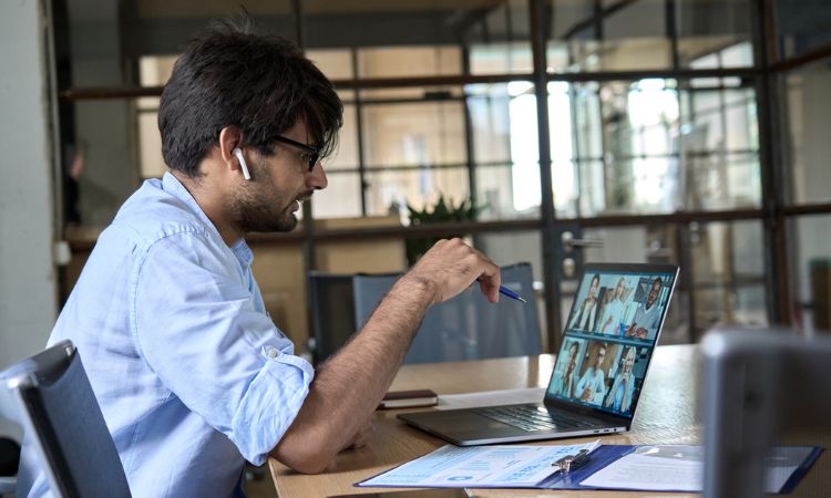 man sitting at a laptop with earbuds in talking in a video conference meeting